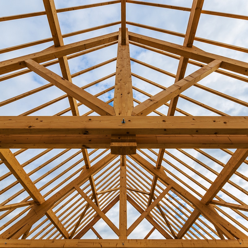 Charpente en bois d'un toit d'une nouvelle construction, vue de dessous avec le ciel nuageux en arrière-plan.