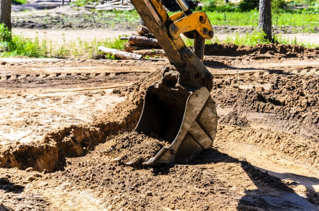 Gros plan sur la benne d'une pelle mécanique jaune creusant profondément dans la terre marron. Un chantier ensoleillé.