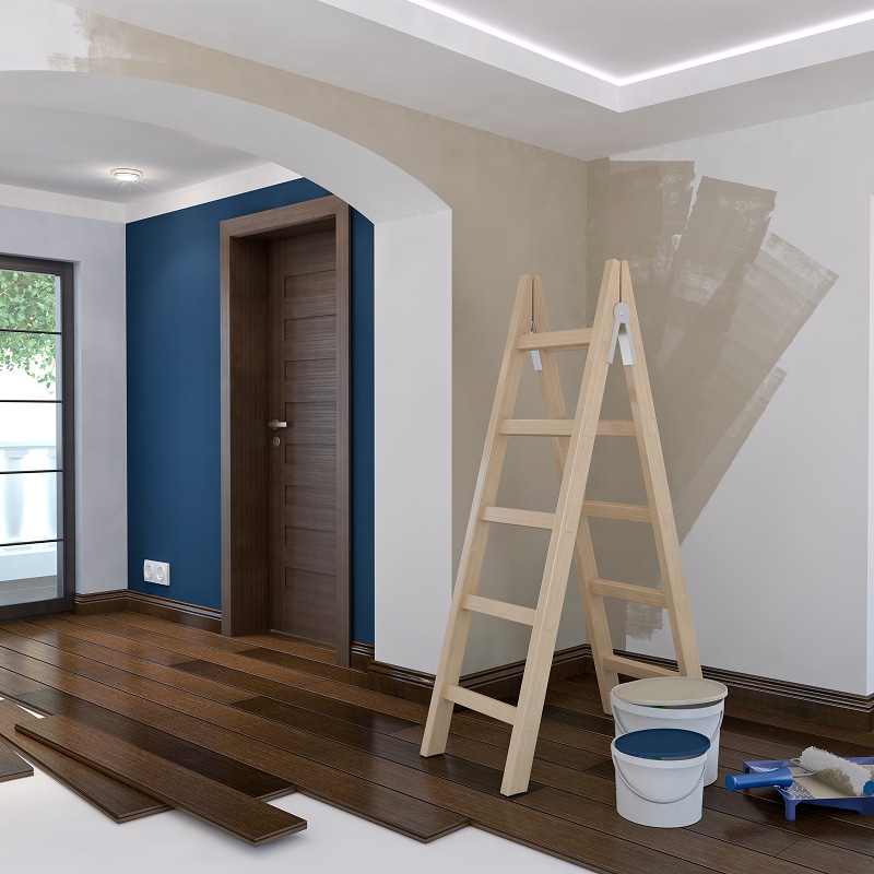 Pièce en rénovation: mur bleu, parquet foncé en pose. Échelle, pots de peinture beige et bleu prêts pour la finition.